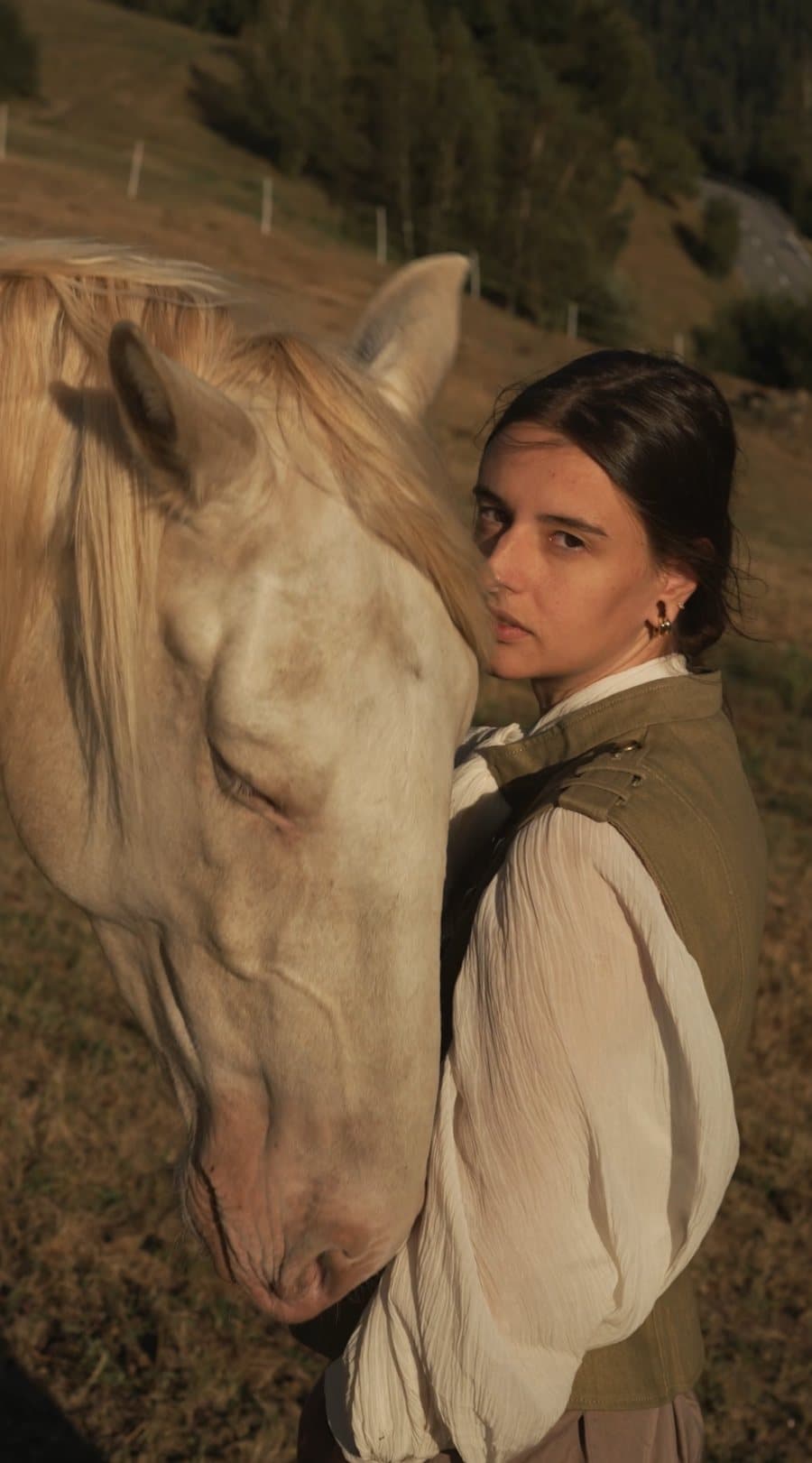 Editorial film still: woman resting against a palomino horse at golden hour